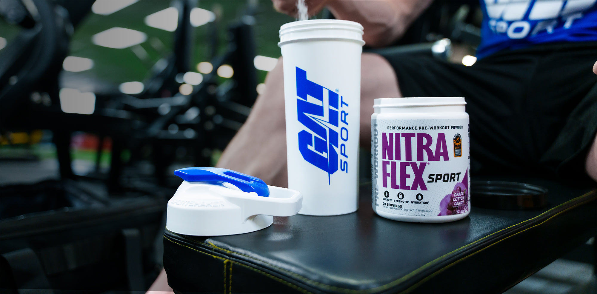 Nitraflex Sport supplement container with GAT Sport shaker on a workout bench with a person in the background.